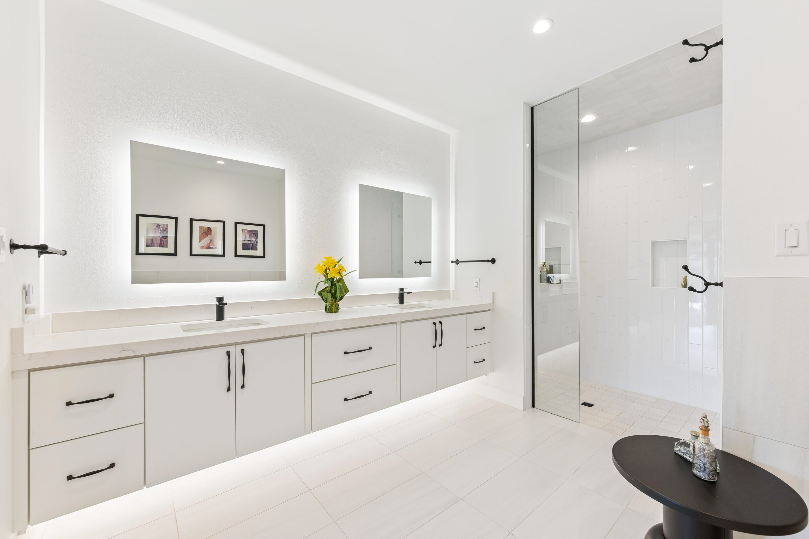 Primary bath with backlit vanity mirrors and glass shower